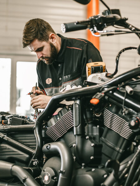 Motorcycle mechanic repairing electronics sports black bike. Handsome mechanic working in auto repair shop.